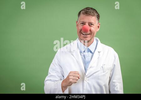 Wissenschaftler mit weißem Mantel hat rote Clownnase auf und steht vor grünem Hintergrund Stockfoto
