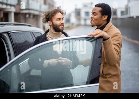 Zwei Männer flirten, während sie in der Nähe des Autos auf der Straße standen Stockfoto