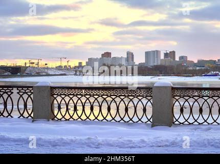 Bezirk Gorsky von Michaels Uferpromenade im Winter. Metallzaun des ob-Ufers, abends neue Häuser in der Ferne. Nowosibirsk, Sibirien Stockfoto