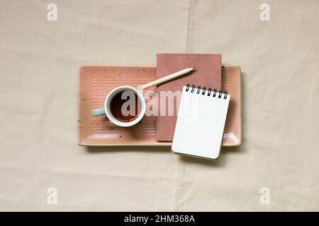 Notizblock und Tasse Kaffee auf beigefarbenem Stoffhintergrund. Draufsicht, Kopierraum Stockfoto