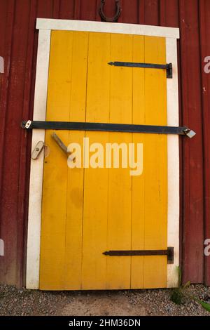 Eine gelbe Tür an einem roten Holzhaus in schweden, verschlossen mit zwei großen Schlössern. Stockfoto