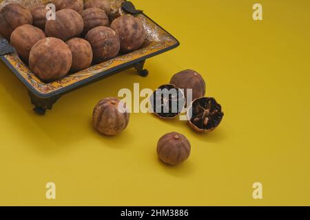 Sonnengetrocknete Bio-Loomi oder Black Lime, Black Lemon, Omani Lemon in antiquarischen orientalischen Teller auf gelbem Hintergrund. Stockfoto