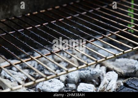 Glühende Holzkohle und Grillrost sind für das Kochen bei Temperatur. Nahaufnahme. Vorderansicht. Schmutziger Grill nach dem Kochen. Schräge Ansicht von vorne. Stockfoto