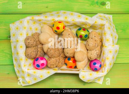 Brötchen und bunte ostereier in einem Korb auf einem grünen Holztisch Stockfoto