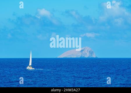 Weiße Segelyacht segelt vor der felsigen Insel Stockfoto