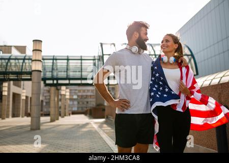 Portrait eines jungen glücklichen Fitness-Paares, das draußen gemeinsam Sport macht und Spaß hat mit USA-Flagge. Stockfoto