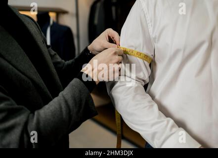 Altmodischer Schneider, der vom Kunden im Atelier Messungen am Handgelenk vorgenommen hat, um einen individuellen klassischen Anzug mit Jacke zu erstellen Stockfoto