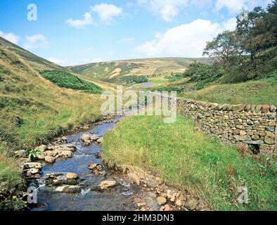 Malerischer plätschernder Bach, der an einer trockenen Steinmauer entlang des ländlichen Hügels in der Landschaft des Waldes von Bowland in Lancashire England, Großbritannien, abstürzt Stockfoto