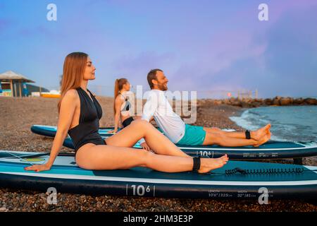 Sommerzeit. Eine Gruppe junger Leute, die am Strand auf Brettern sitzen. Erholung mit Freunden. Surfen und Aktivitäten. Stockfoto