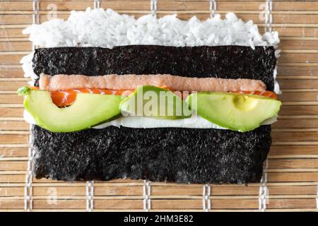 Zutaten von Sushi Rollen bereit zum Einwickeln auf der Bambusmatte. Stockfoto