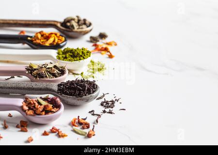 Verschiedene Arten von trockenem Tee in Löffeln auf weißem Marmorboden, Kopierraum. Grüner Tee, Matcha, Zitrustee, schwarzer Tee und Kräuterentgiftungstee. Stockfoto