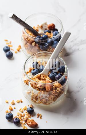 Müsli mit Nüssen, Joghurt und Beeren in einem Glas. Frühstücksparfait mit Müsli, Joghurt und Heidelbeeren, weißer Hintergrund. Stockfoto