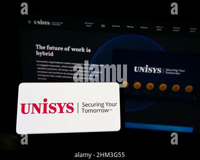 Person, die Mobiltelefon mit dem Logo des US-AMERIKANISCHEN IT-Unternehmens Unisys Corporation auf dem Bildschirm vor der Business-Webseite hält. Konzentrieren Sie sich auf die Telefonanzeige. Stockfoto