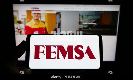 Person mit Mobiltelefon und Logo des mexikanischen Unternehmens Fomento Econmico Mexicano (FEMSA) auf dem Bildschirm vor der Webseite. Konzentrieren Sie sich auf die Telefonanzeige. Stockfoto