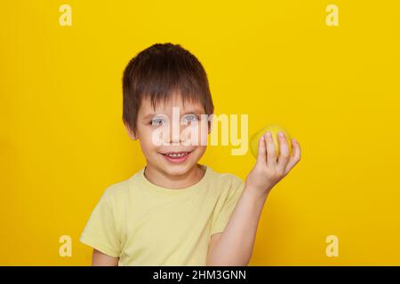 Ein fröhliches Kind in einem gelben T-Shirt auf gelbem Hintergrund hält einen Apfel in den Händen. Das Konzept der gesunden Ernährung für Kinder. Speicherplatz kopieren Stockfoto