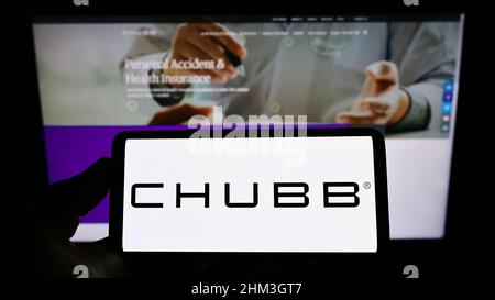 Person, die Mobiltelefon mit Logo der Schweizer Versicherungsgesellschaft Chubb Limited auf dem Bildschirm vor der Business-Webseite hält. Konzentrieren Sie sich auf die Telefonanzeige. Stockfoto