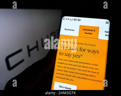 Person, die Mobiltelefon mit der Website der Schweizer Versicherungsgesellschaft Chubb Limited auf dem Bildschirm vor dem Logo hält. Konzentrieren Sie sich auf die Mitte des Telefondisplays. Stockfoto