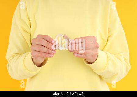 Frau hält Hörgeräte auf gelbem Hintergrund Stockfoto