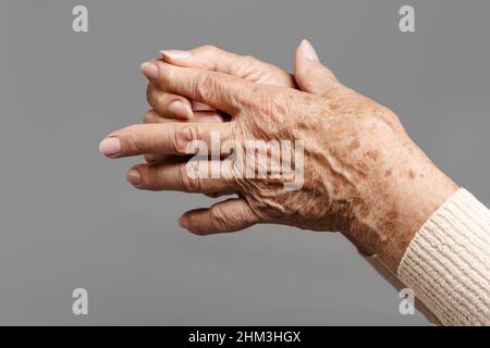 Eine ältere Frau massiert ihre Finger und hat Schmerzen in den Gelenken. Grauer Hintergrund, Nahaufnahme der Hände. Das Konzept von Rheuma und Arthritis. Stockfoto