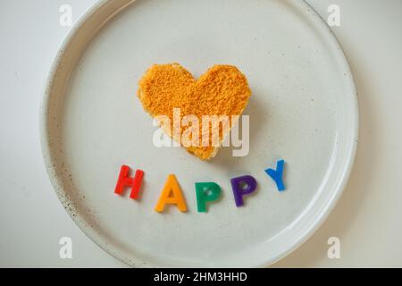 regenbogen Farben und Wort glücklich in der Nähe orange herzförmigen Kuchen. LGBT-Stil Ausdruck von Liebe Leidenschaft. Stockfoto