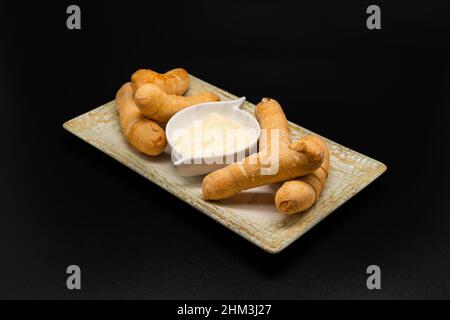 Venezolanischer Tequenos gefüllt mit Käse mit Sauce auf schwarzem Hintergrund. Stockfoto