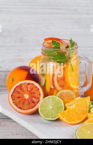 Wasser aus Zitrusfrüchten und Kräutern zur Entgiftung oder Diät in Glasflaschen auf Holzbrett, weißer Hintergrund. Limetten und Orangen. Sauber essen, Gewicht zu verlieren, ist es Stockfoto