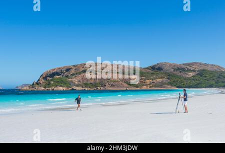 Junger Mann fotografiert eine junge Frau, die am Strand der berühmten Hellfire Bay, Cape Le Grand, in der Nähe von Esperance, Westaustralien, mit einem Fußballspiel spielt Stockfoto