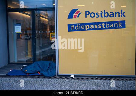 05.02.2022, Berlin, Deutschland, Europa - Obdachloser schläft in seinem Schlafsack auf dem Bürgersteig vor einer Postbank-Filiale in der Innenstadt. Stockfoto