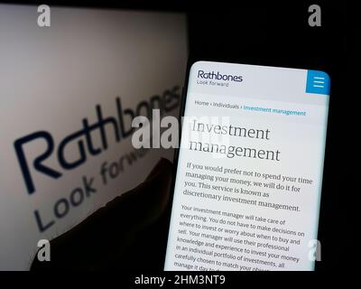 Person mit Mobiltelefon und Webseite des britischen Finanzunternehmens Rathbones Group plc auf dem Bildschirm mit Logo. Konzentrieren Sie sich auf die Mitte des Telefondisplays. Stockfoto