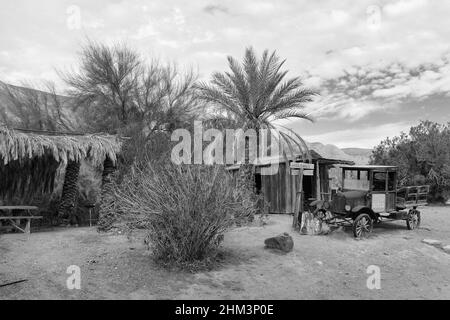 Alter Lieferwagen, Scheune und Dattelpalme auf der China Ranch Date Farm, Tecopa, Kalifornien. Schwarzweiß-Foto. Stockfoto