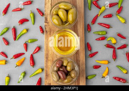 Komposition mit Chilischoten, Oliven und Olivenöl auf grauem Hintergrund Stockfoto