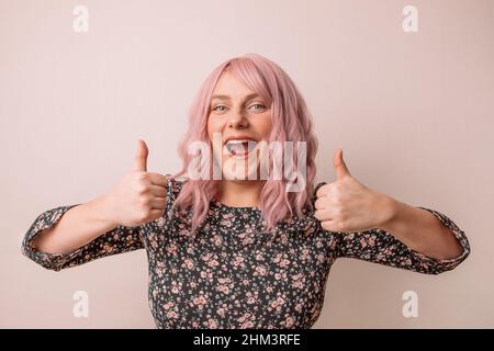 Banner zu Aufmerksamkeitsaktionen. Charmante junge kaukasische Frau mit rosa Haaren in einem schönen Frühling hellen Kleid zeigt Daumen nach oben wie Geste isoliert Stockfoto