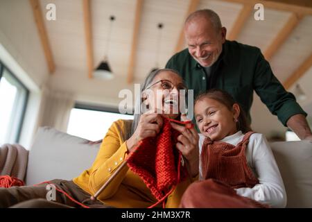 Großmutter sitzt auf dem Sofa und lehrt ihre Enkelin, wie man zuhause im Haus strickt. Stockfoto