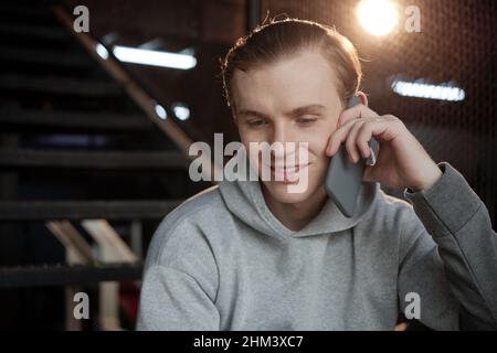 Porträt eines lächelnden jungen Fitness-Trainers im Hoodie, der mit dem Kunden telefoniert Stockfoto