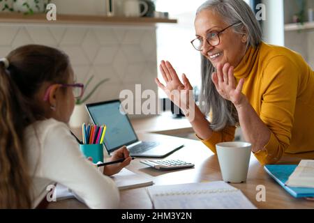 Kleines Mädchen mit älterer Großmutter, die zu Hause Mathe-Hausaufgaben macht. Stockfoto