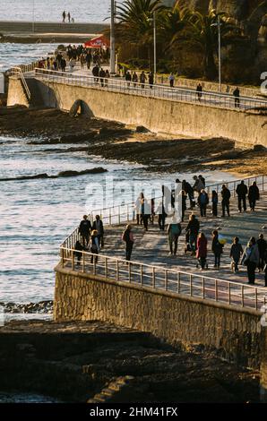 Cascais, Portugal - 5. Februar 2022: Blick aus der Perspektive auf die Menschen an der Promenade am Poca Beach, einem kleinen, sandigen Stadtstrand mit felsigen Gebieten Stockfoto