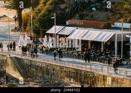 Cascais, Portugal - 5. Februar 2022: Blick aus der Perspektive auf die Menschen an der Promenade am Poca Beach, einem kleinen, sandigen Stadtstrand mit felsigen Gebieten Stockfoto