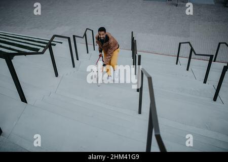 Blick aus der Höhe auf einen glücklichen jungen Mann, der mit seinem Hund im Freien in der Stadt nach oben läuft. Stockfoto