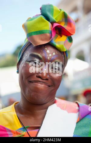 Porträt einer lächelnden Frau, die einen textilen Kopfschmuck trägt, während sie während des Karnevals auf den Seychellen auf der Straße auftrat. Stockfoto