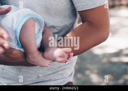 Nahaufnahme eines Vaters, der sein Kleinkind mit einer Windel in den Armen im Freien hält. Unterer Teil des Kindes. Selektiver Fokus. Stockfoto