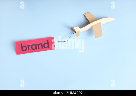 Erfolg der Business Branding Kampagne und Startkonzept. Flugzeug fliegt mit Markenschild auf blauem Hintergrund mit Kopierraum. Stockfoto