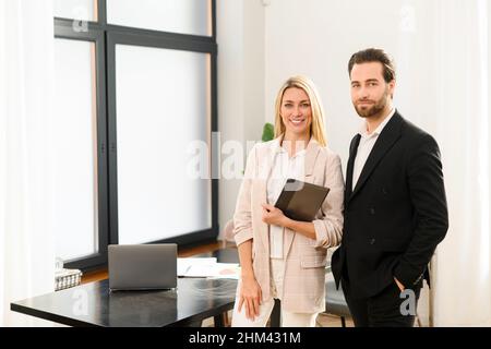 Junge schöne Team von Mann und Frau ist mit digitalen Tablet, während im Büro stehen. Sie halten das Tablet in den Händen, blicken auf die Kamera und lächeln Stockfoto
