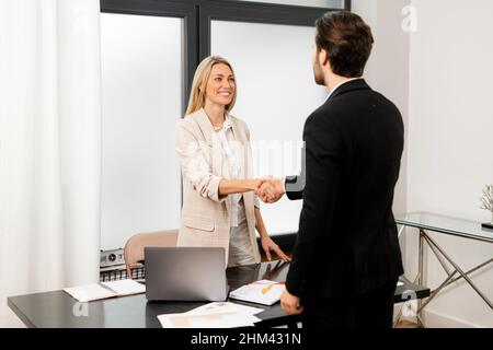 Große Sache. Angenehme junge, selbstbewusste Geschäftsfrau und Geschäftsfrau in formeller Kleidung stehen gegenüber und schütteln sich die Hände. Stock Foto Stockfoto