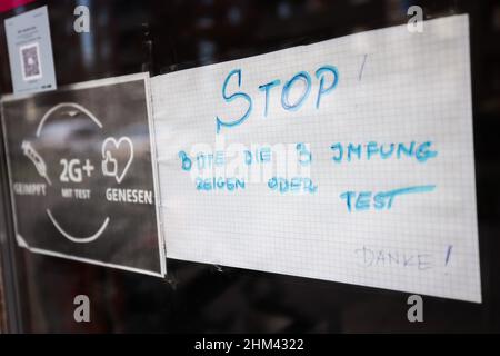 07. Februar 2022, Hamburg: Ein Schild mit der Aufschrift „Stop! Bitte zeigen Sie 3 Impfungen oder Tests an - Vielen Dank!' Und „geimpft, 2G+ mit Test, erholt“ hängt neben der Eingangstür eines Cafés im Stadtteil Hamburg-Veddel. Foto: Christian Charisius/dpa Stockfoto