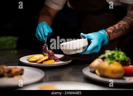 Die Hände des Küchenchefs in Handschuhen dienen und dekorieren das Essen in der Restaurantküche Stockfoto