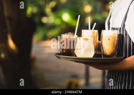 Der Kellner trägt eine Schürze und serviert Eiskaffee und ein kühles Getränk auf einem Tablett Stockfoto
