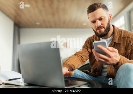 Ernsthafter Freiberufler, Der Zu Hause Telefon Und Laptop Benutzt Stockfoto