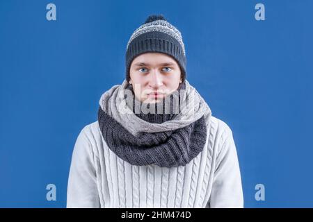 Winter. Winterkleidung. Ein Mann in einem weißen Pullover, Schal und Winterhut sitzt ruhig und blickt auf die Kamera. Stockfoto