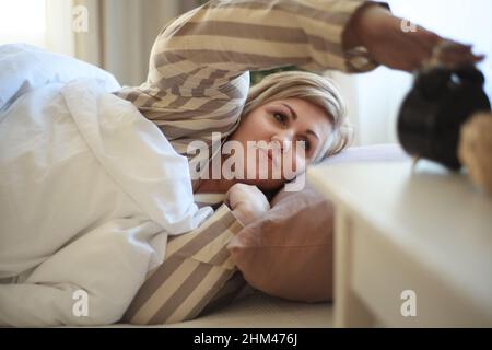 Übergewichtige Frau, die im Bett aufwacht und zu Hause den Wecker abschaltet. Stockfoto