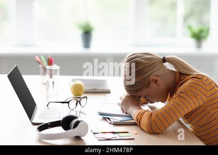 Traurige müde kaukasische Teenager-Mädchen blond legte ihren Kopf auf den Tisch ruhen aus Studie in minimalistischen Küche Interieur Stockfoto